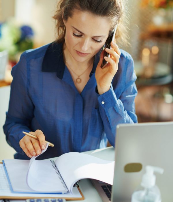stylish woman in blue blouse in the modern house in sunny day using a mobile phone and working in temporary home office during the coronavirus epidemic.